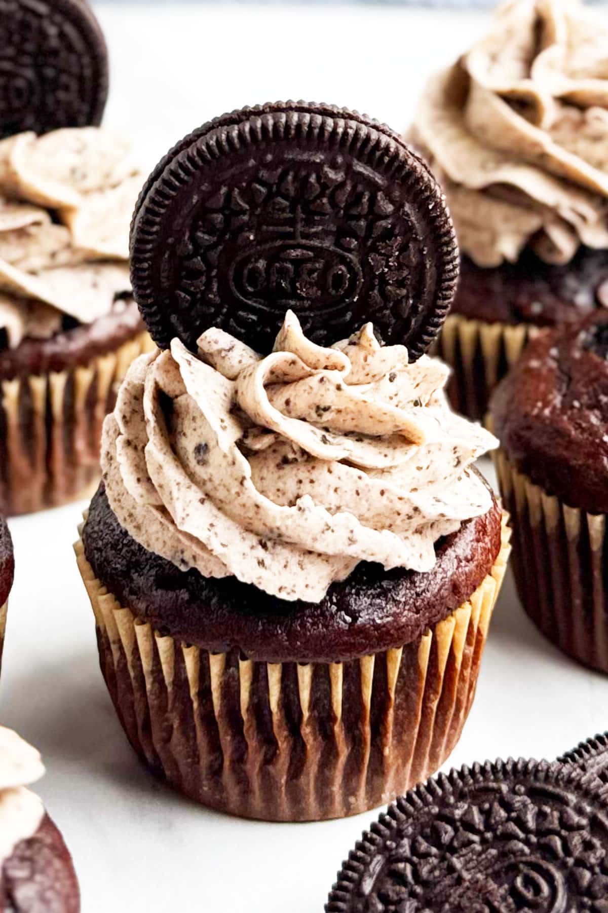 Easy chocolate Oreo cupcakes with cake mix and cookie bottom that is topped with cookies and cream buttercream frosting on white marble background.