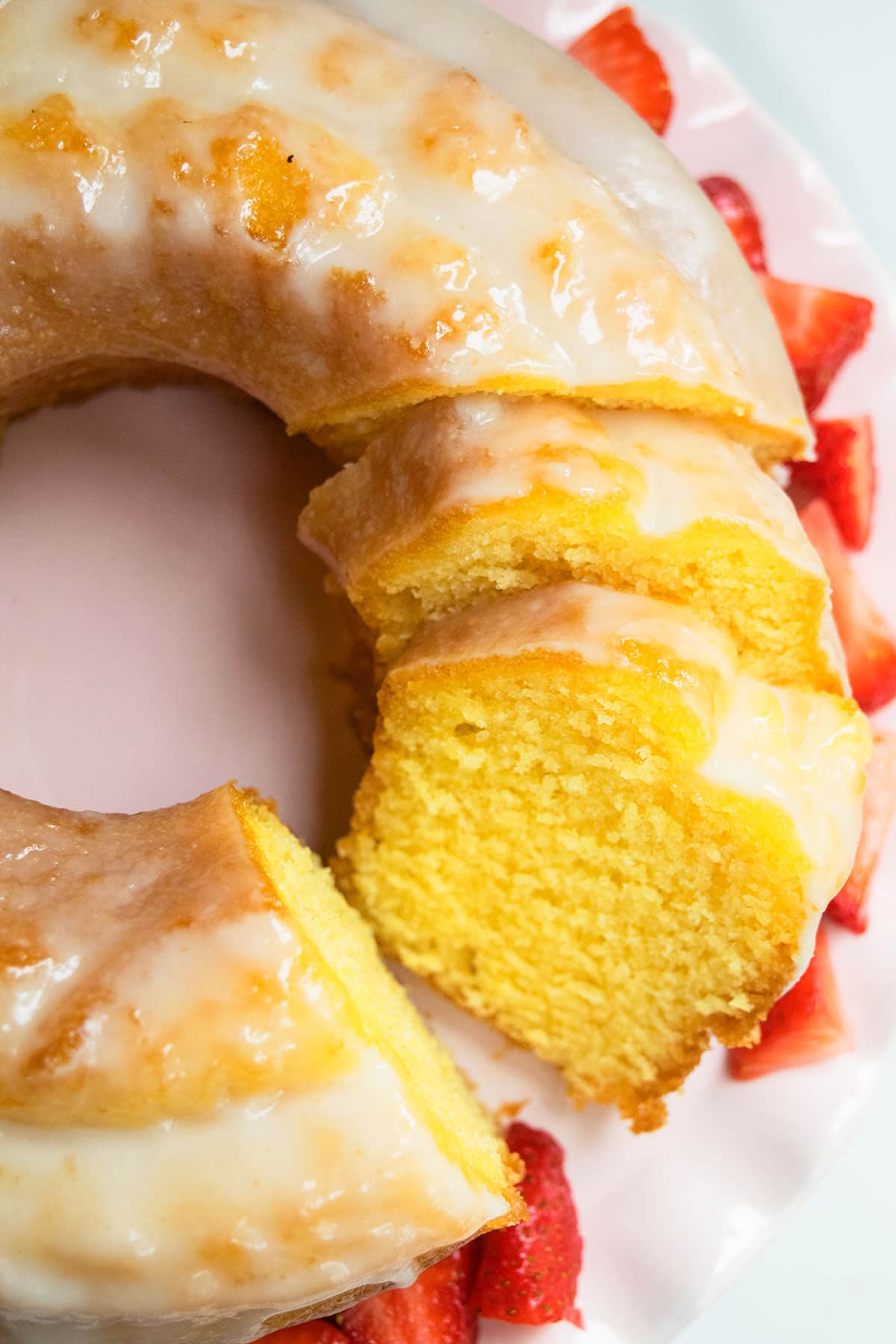 Sliced glazed bundt cake on light pink dish. 