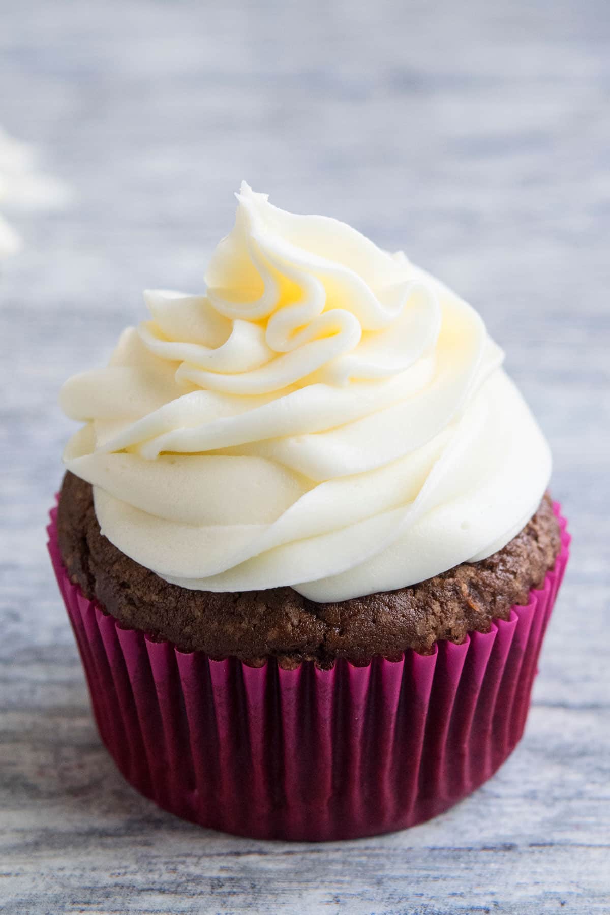 Swirl of vanilla icing on top of chocolate cupcake with pink liner. 