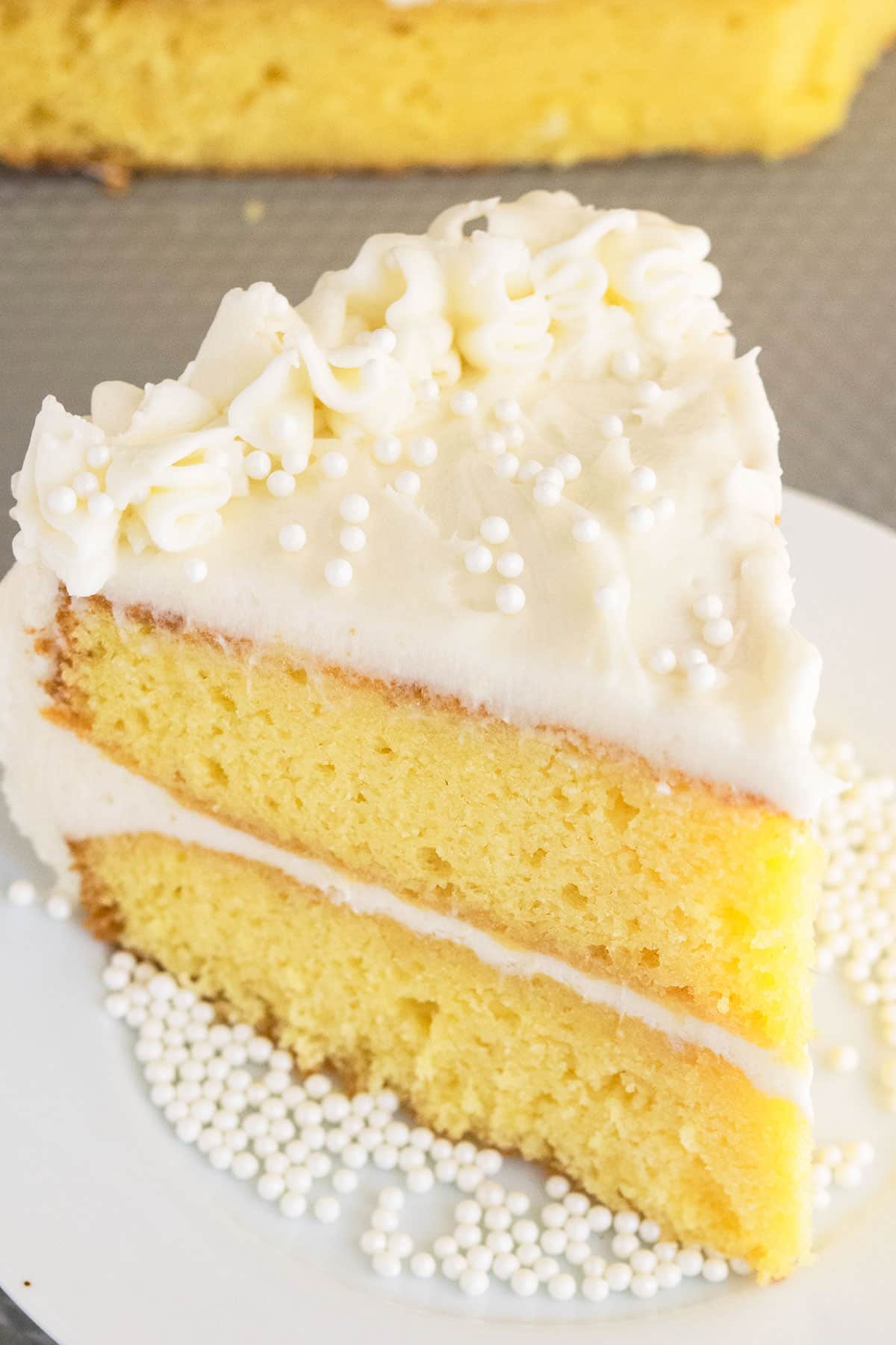 Slice of best moist vanilla cake with American buttercream frosting on white cake dish. 