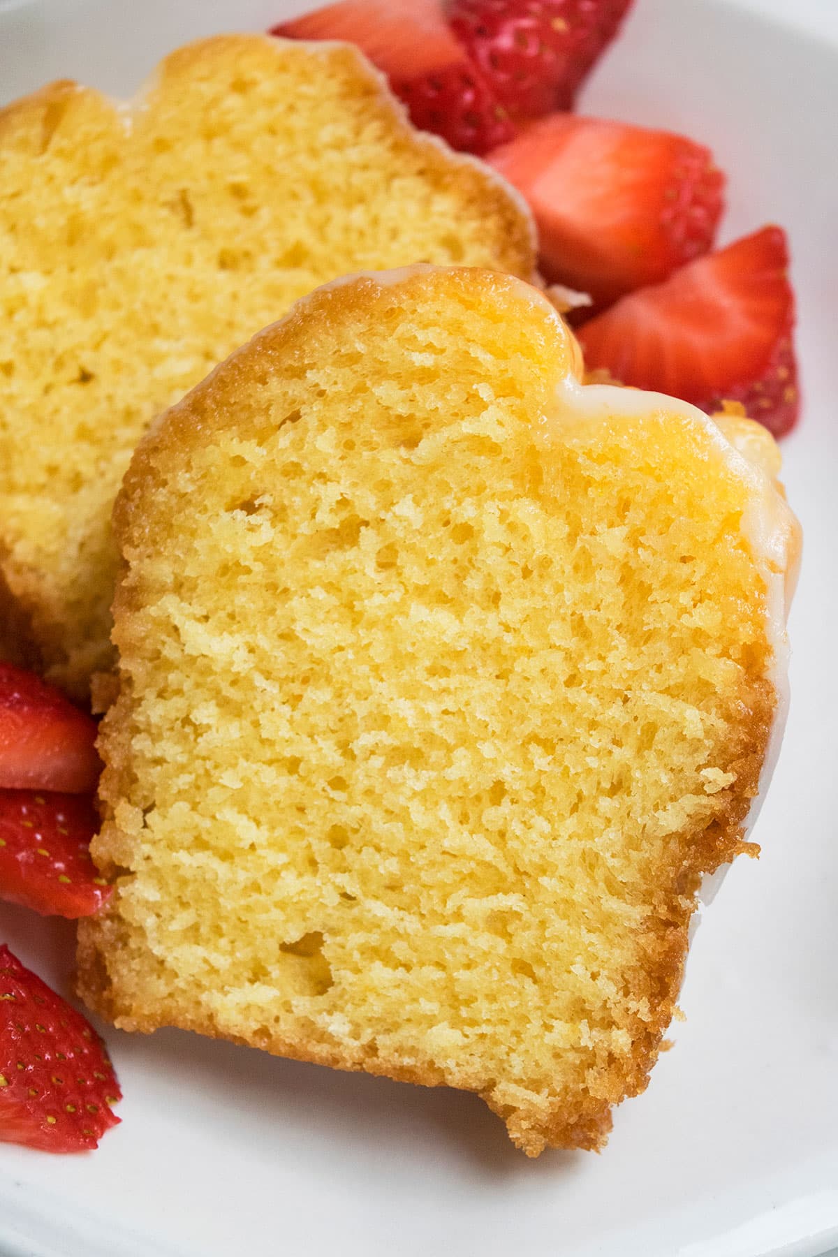 Closeup Shot of slice of glazed cake on white dish with fresh strawberries. 