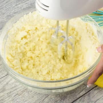 Ingredients being mixed together in glass bowl with hand held mixer. 