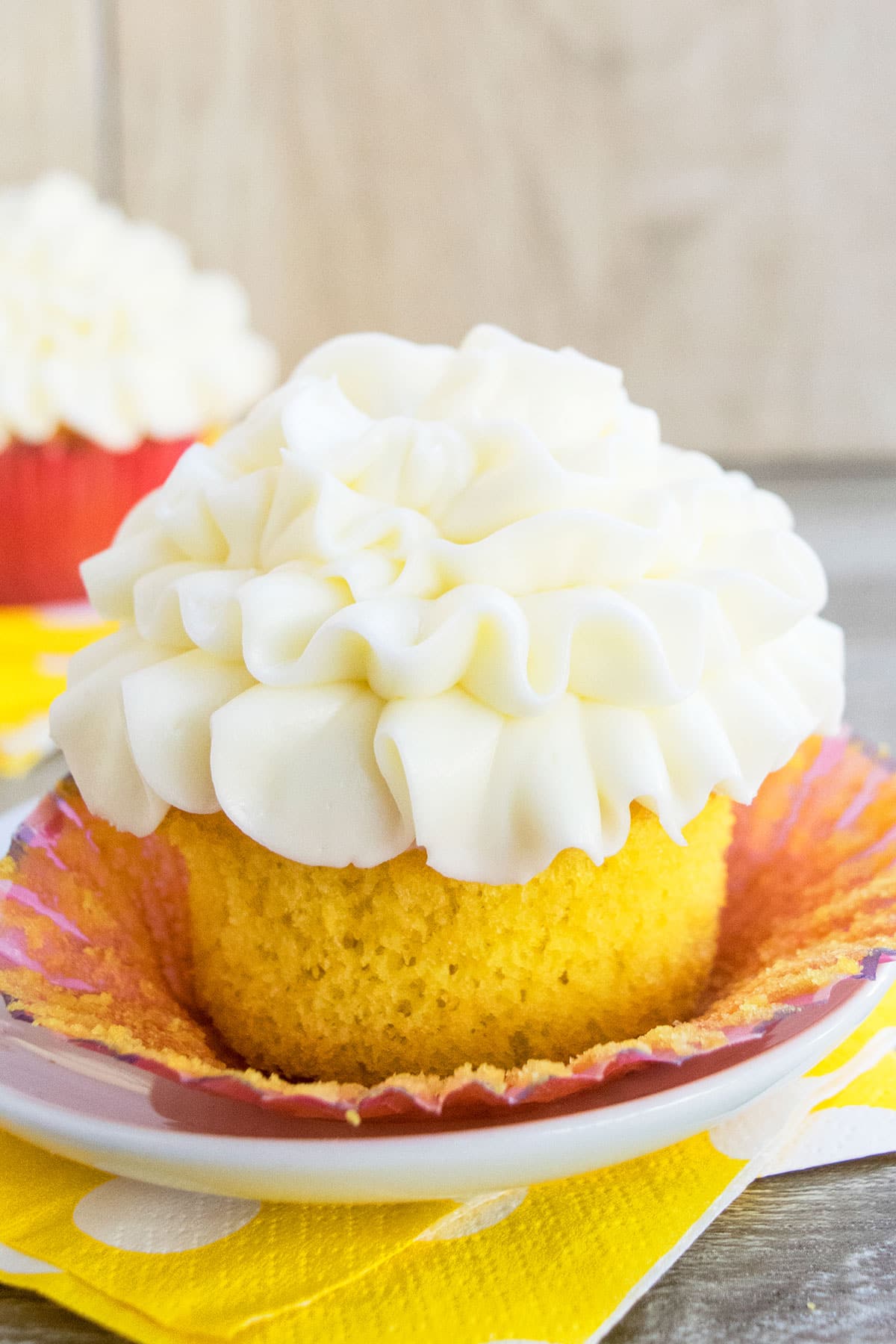 Soft and moist lemon cupcakes with lemon curd filling and cream cheese frosting on white dish- Liner partially removed. 