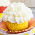 Easy, soft and moist lemon cupcakes from scratch with lemon curd filling and cream cheese frosting on white dish- Liner partially removed.