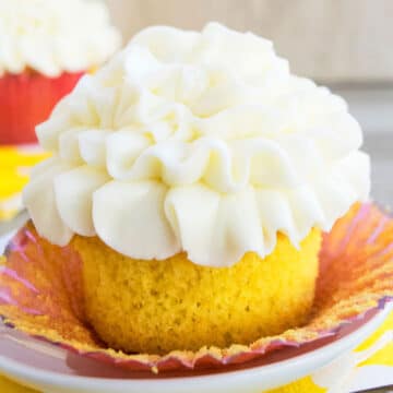 Easy, soft and moist lemon cupcakes from scratch with lemon curd filling and cream cheese frosting on white dish- Liner partially removed.
