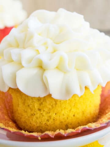 Easy, soft and moist lemon cupcakes from scratch with lemon curd filling and cream cheese frosting on white dish- Liner partially removed.