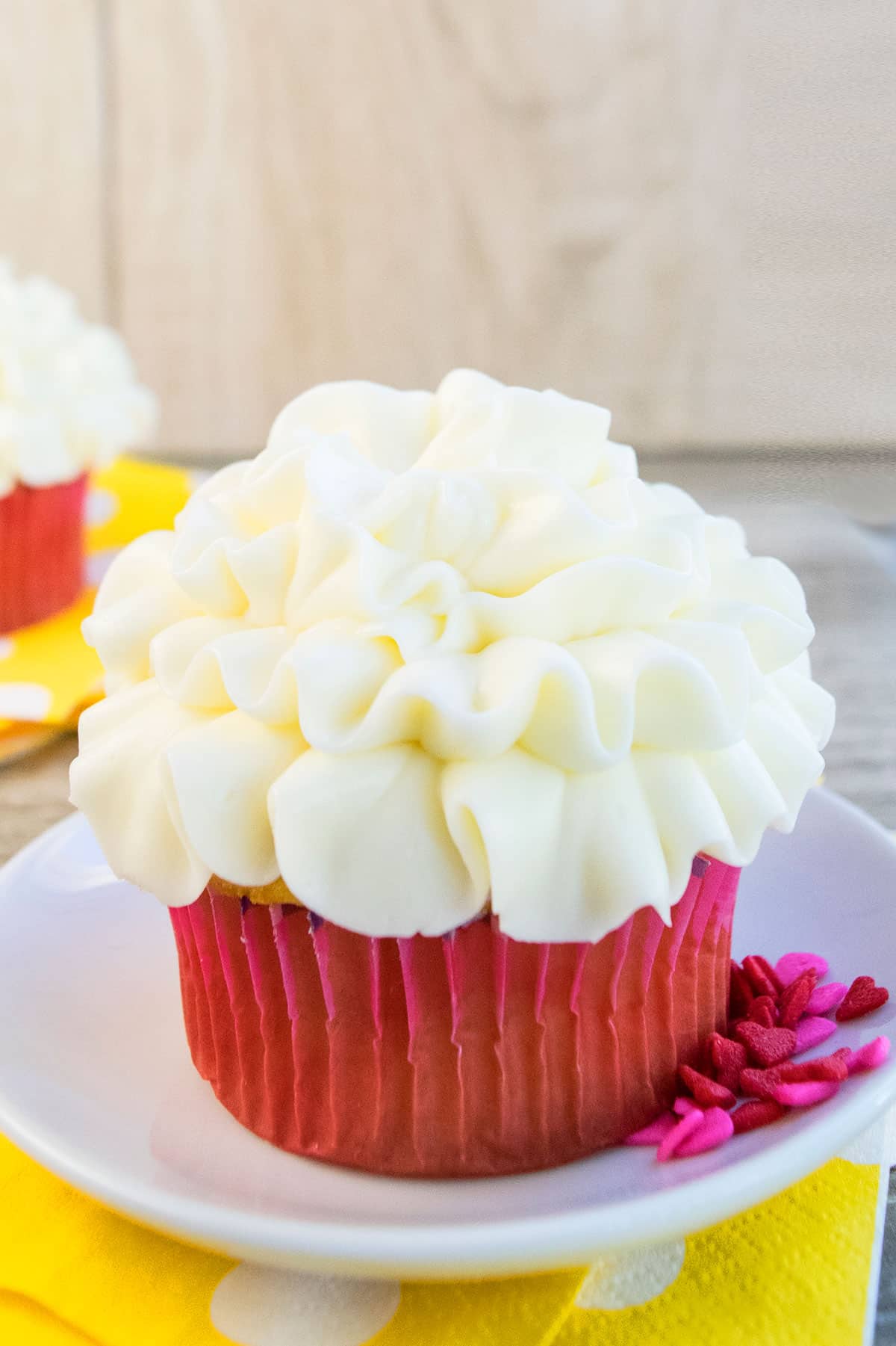 Tall frosted cupcake with pink liner on white dish.