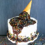 Best easy homemade ice cream cake with melting ice cream cone and sprinkle decoration on top on white cake stand.