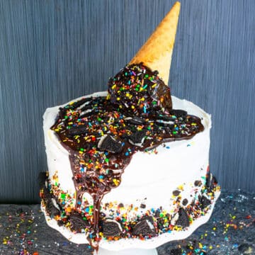 Best easy homemade ice cream cake with melting ice cream cone and sprinkle decoration on top on white cake stand.