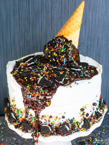 Best easy homemade ice cream cake with melting ice cream cone and sprinkle decoration on top on white cake stand.