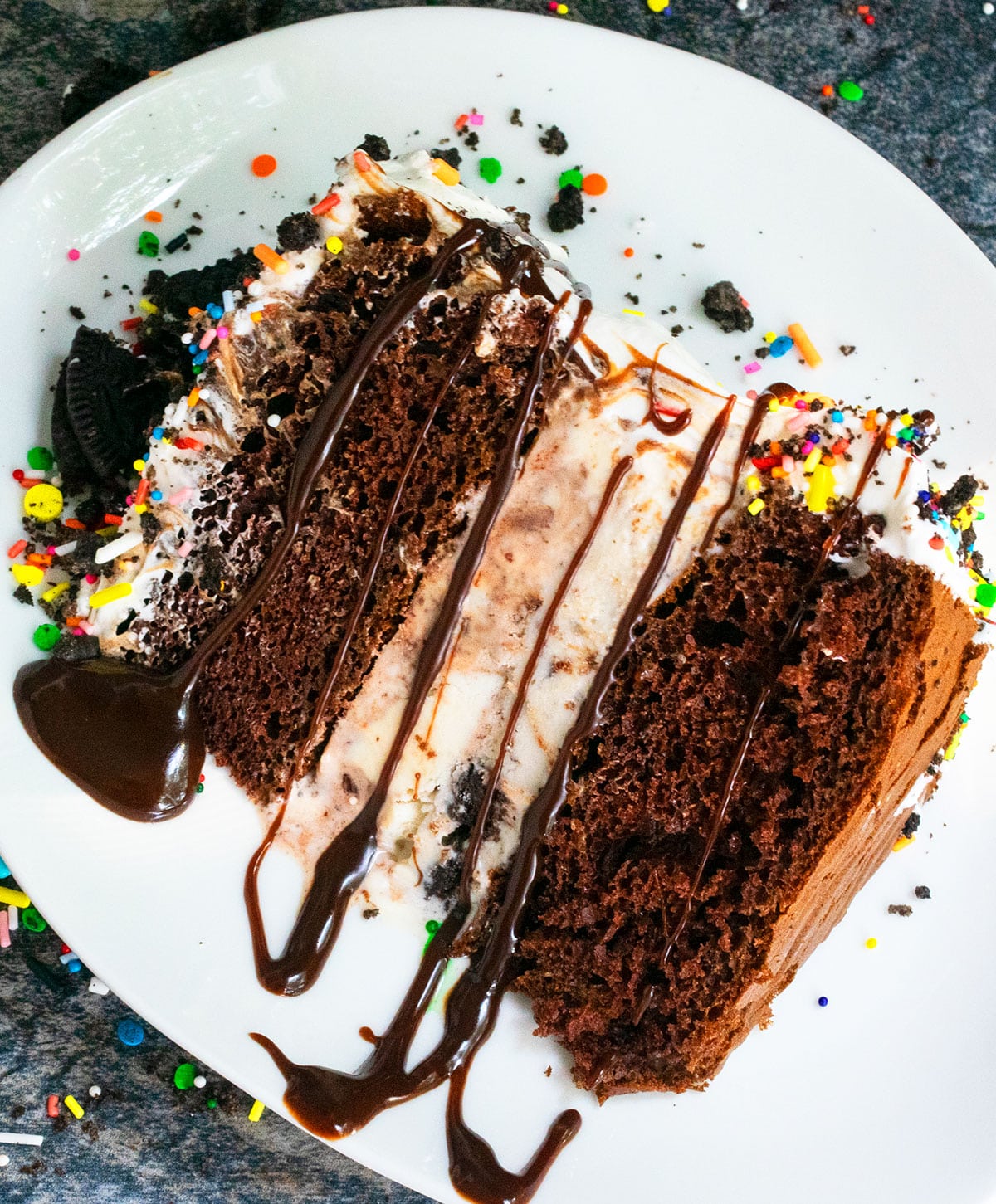 Slice of cake with ganache drizzle and sprinkles on white dish. 