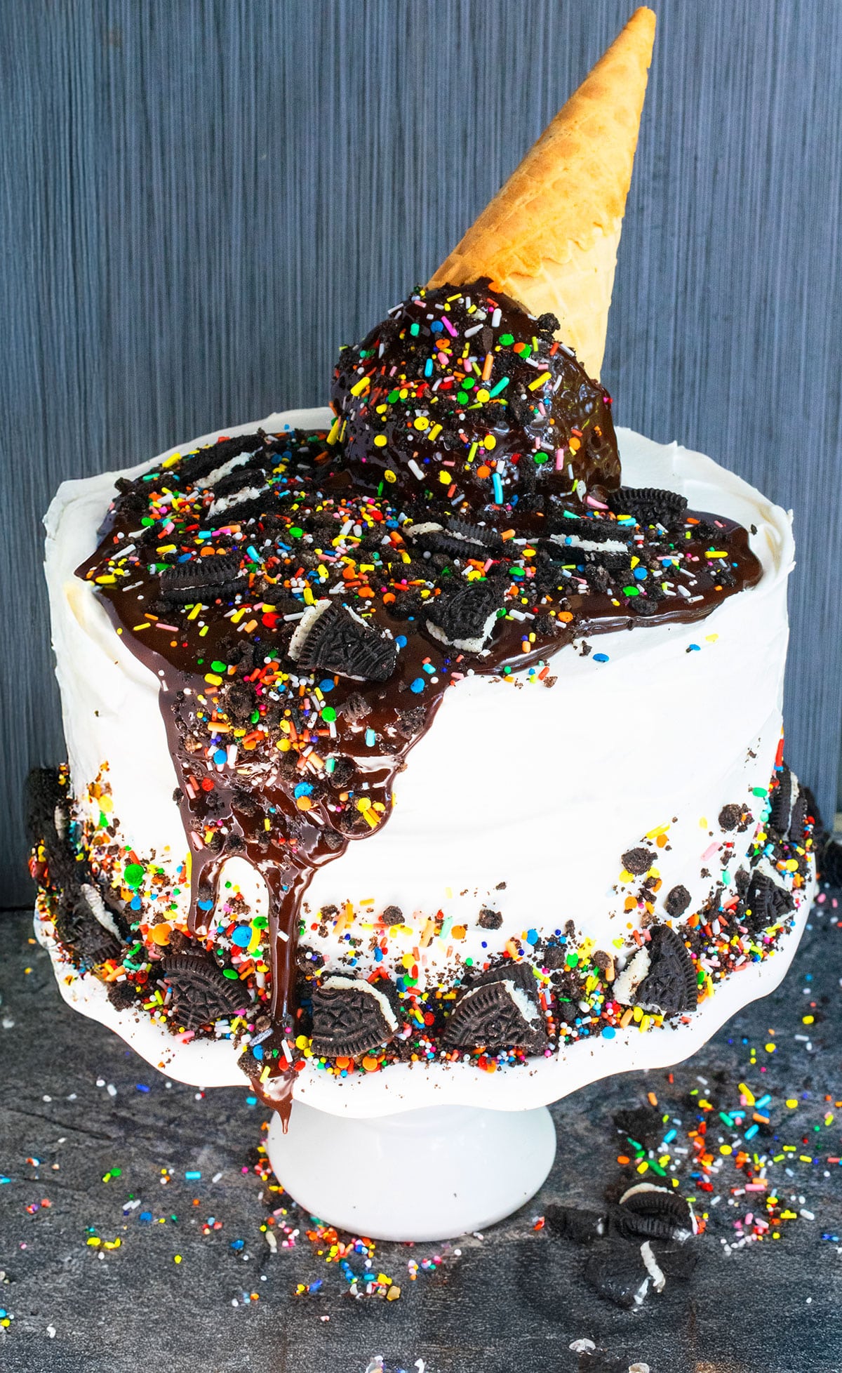Best easy homemade ice cream cake with melting ice cream cone and sprinkle decoration on top placed on white cake stand. 