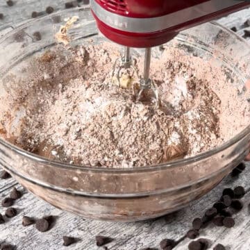 Cocoa powder and powdered sugar added to butter mixture in glass bowl. 