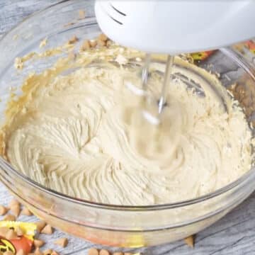 Smooth peanut butter mixture in glass bowl with hand held mixer. 