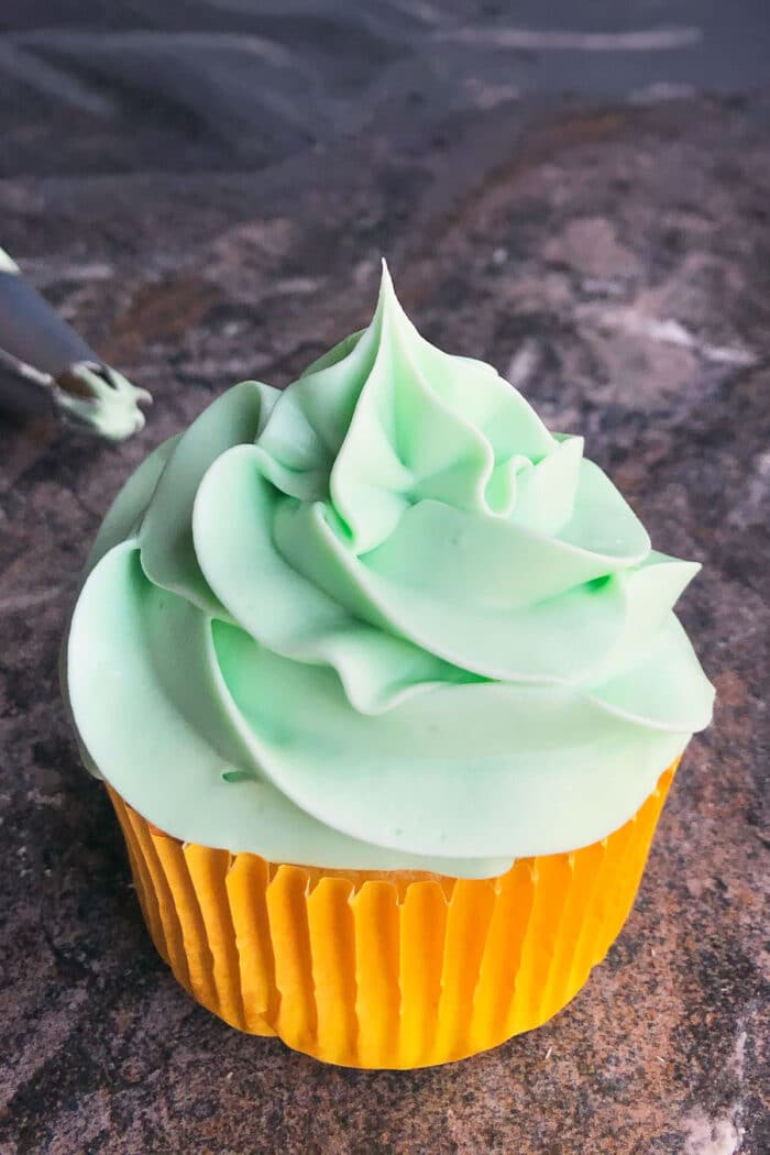 Mint frosting piped on top of cupcake with yellow liner. 