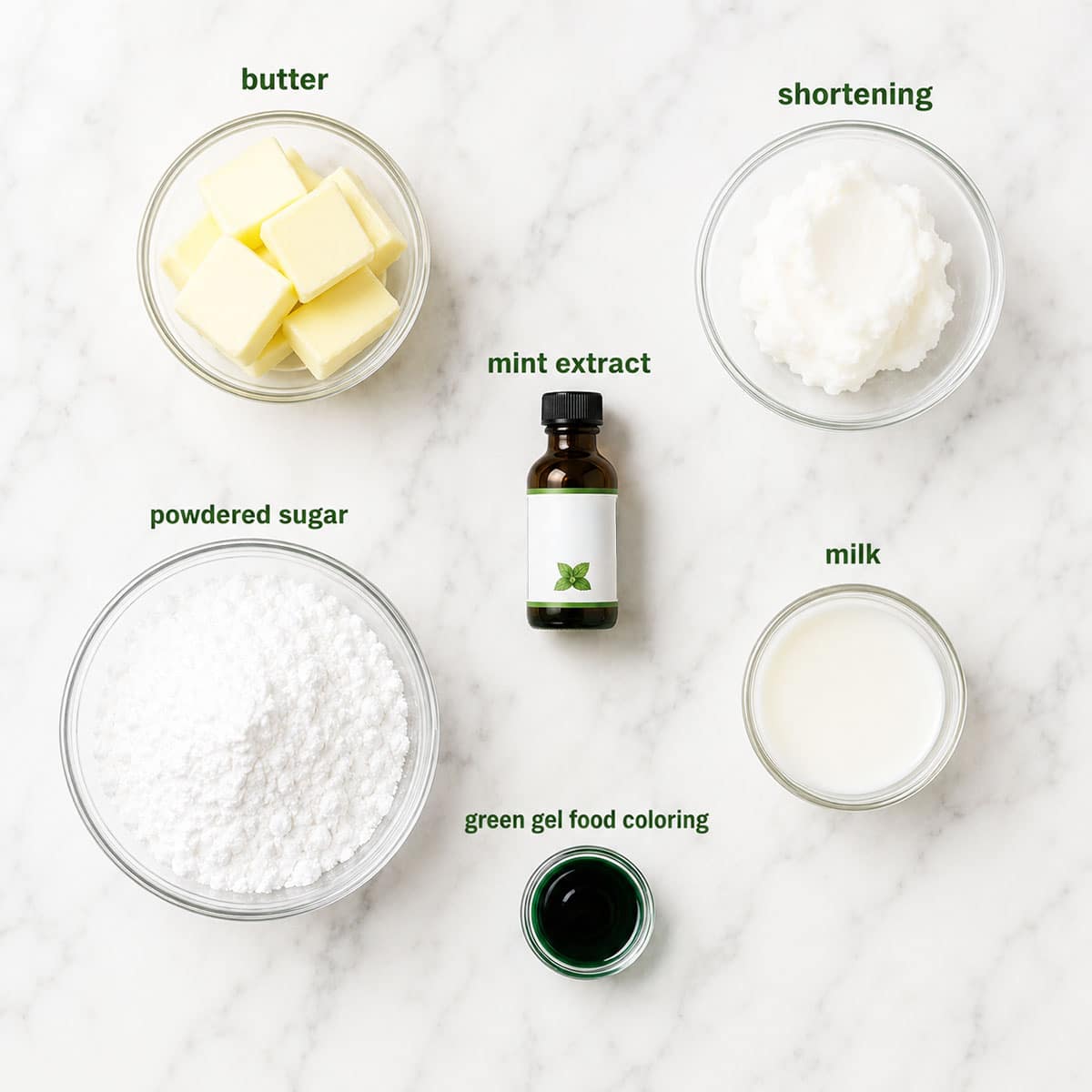 Ingredients for recipe on white marble background- butter, shortening, extract, powdered sugar, milk, food coloring. 
