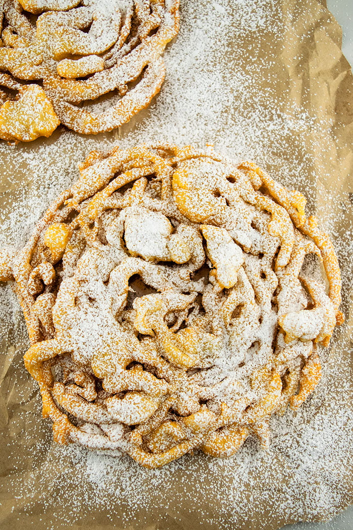 Classic Funnel Cake With Powdered Sugar Topping on Brown Paper Backdrop