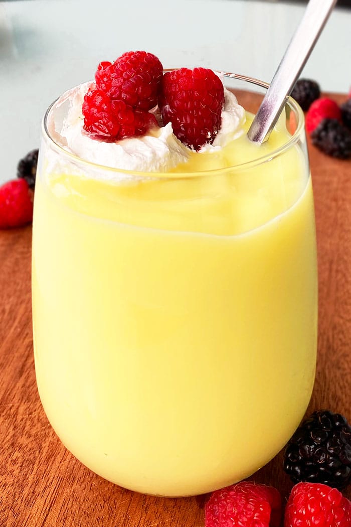 Easy Vanilla Pudding in Clear Glass Cup Topped With Whipped Cream and Raspberries