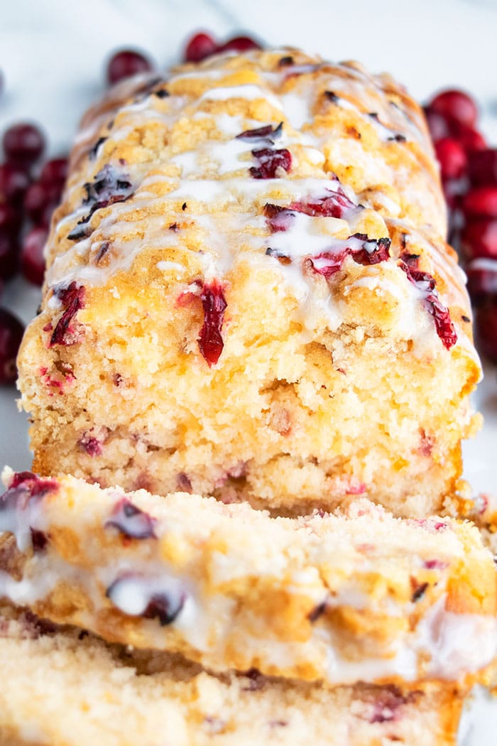 Best Cranberry Bread with Orange Glaze on White Surface with Cranberries Scattered Everywhere