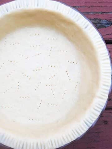 Easy Homemade Flaky Butter Pie Crust in Pie Dish on Rustic Red Wood Background