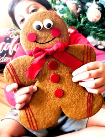 Kid Holding Jumbo Gingerbread Men Cookies With Christmas Decor in Background