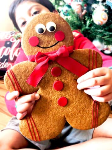 Kid Holding Jumbo Gingerbread Men Cookies With Christmas Decor in Background