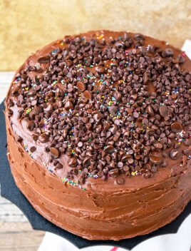 Easy Moist Homemade Triple Chocolate Cake Recipe From Scratch with Chocolate Frosting on Black Stand and Rustic Wood Background