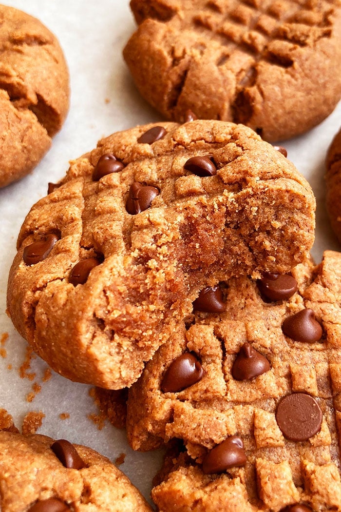 Thick and Soft Peanut Butter Cookies With Chocolate Chips and Cocoa Powder on Parchment Paper- One Bite Removed. 