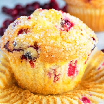 Quick, Soft, Fluffy, Easy Cranberry Orange Muffins on White Background With Liner Partially Removed.