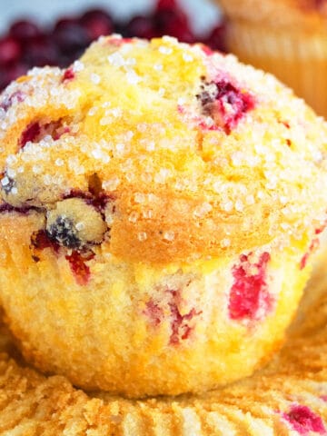 Quick, Soft, Fluffy, Easy Cranberry Orange Muffins on White Background With Liner Partially Removed.