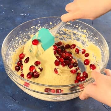 Cranberries being folded into the batter with a spatula. 