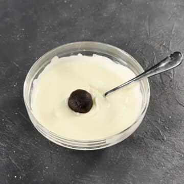 Cookie ball being dipped in melted white chocolate. 