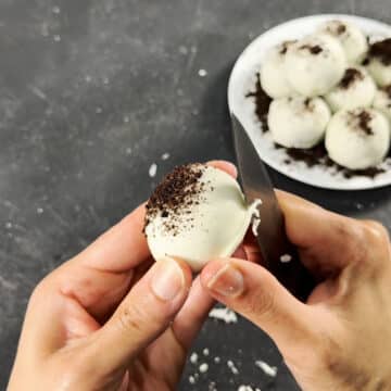 Excess chocolate being cut with a knife along the base of the ball. 