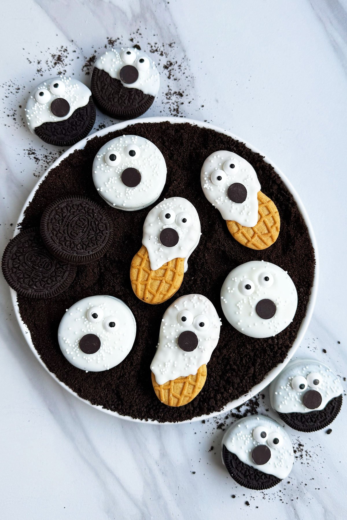 Easy Ghost Cookies With Oreos and Nutter Butter on White Dish With Cookie Crumbs on White Marble Background.