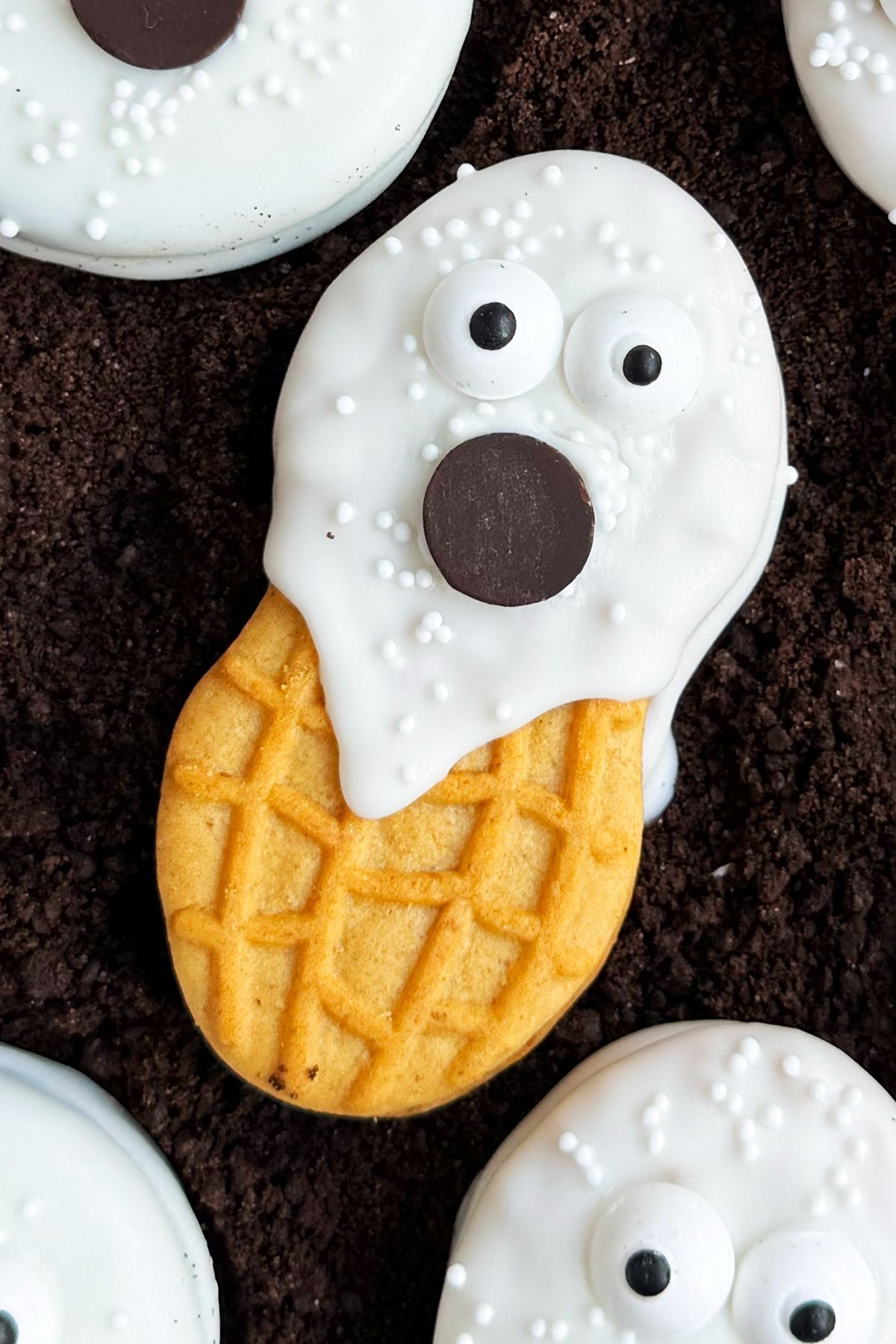 Homemade Chocolate Covered Nutter Butter Ghost Cookies on White Dish of Cookie Crumbs. 