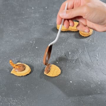 Melted chocolate being spooned on top portion of cookie. 