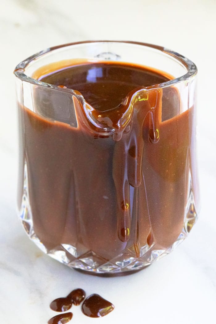 Homemade Chocolate Fudge Sauce in Small Glass Pitcher on White Background