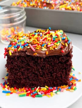 Slice of Easy Chocolate Sheet Cake With Cake Mix Frosted With Fudgy Chocolate Icing And Sprinkles on White Plate