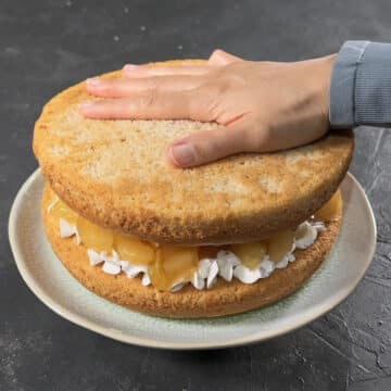 Second cake layer being pressed on top of filling and frosting. 