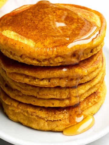 Stack of Easy Pumpkin Pancakes With Maple Syrup on White Dish.