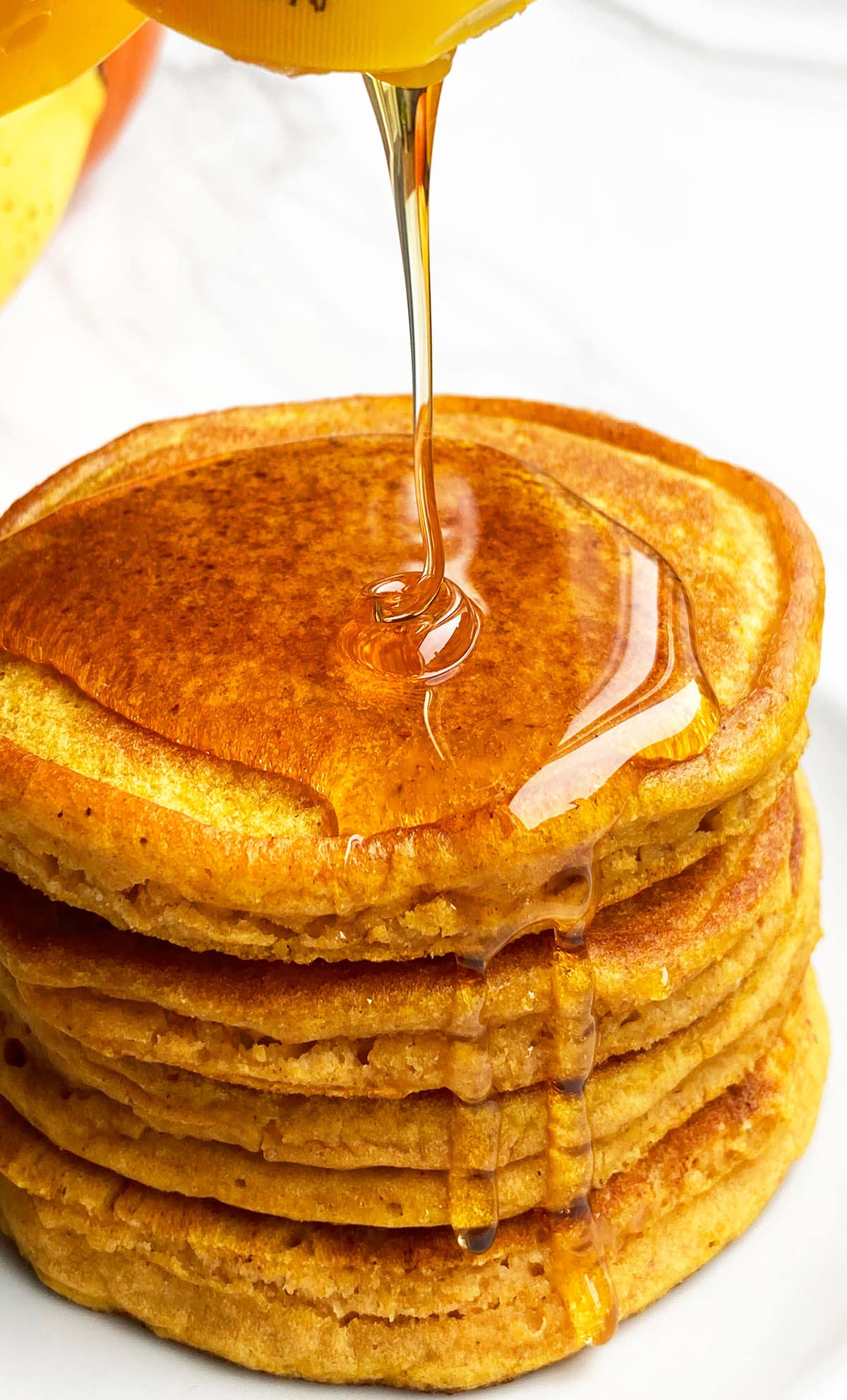 Maple Syrup Being Poured on Stack of Easy Pumpkin Pancakes on White Dish. 