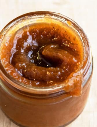 Easy Crockpot Apple Butter In Glass Jar on Rustic Brown Background.