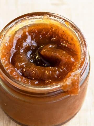 Easy Crockpot Apple Butter In Glass Jar on Rustic Brown Background.