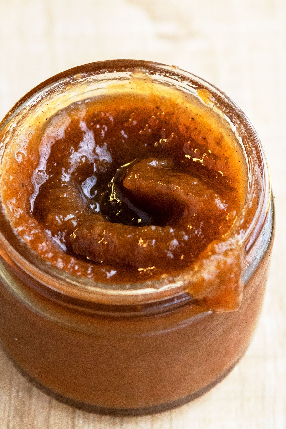 Easy Crockpot Apple Butter In Glass Jar on Rustic Brown Background. 