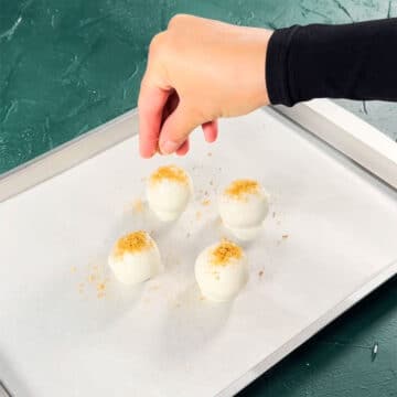 Candy balls being topped off with additional cookie crumbs. 