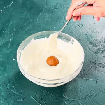 Candy balls being dipped in bowl of melted white chocolate. 