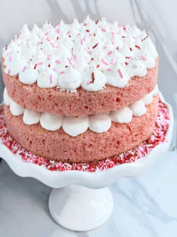 Easy Pink Champagne Cake From Scratch With Whipped Cream Frosting and Sprinkles on White Cake Stand.