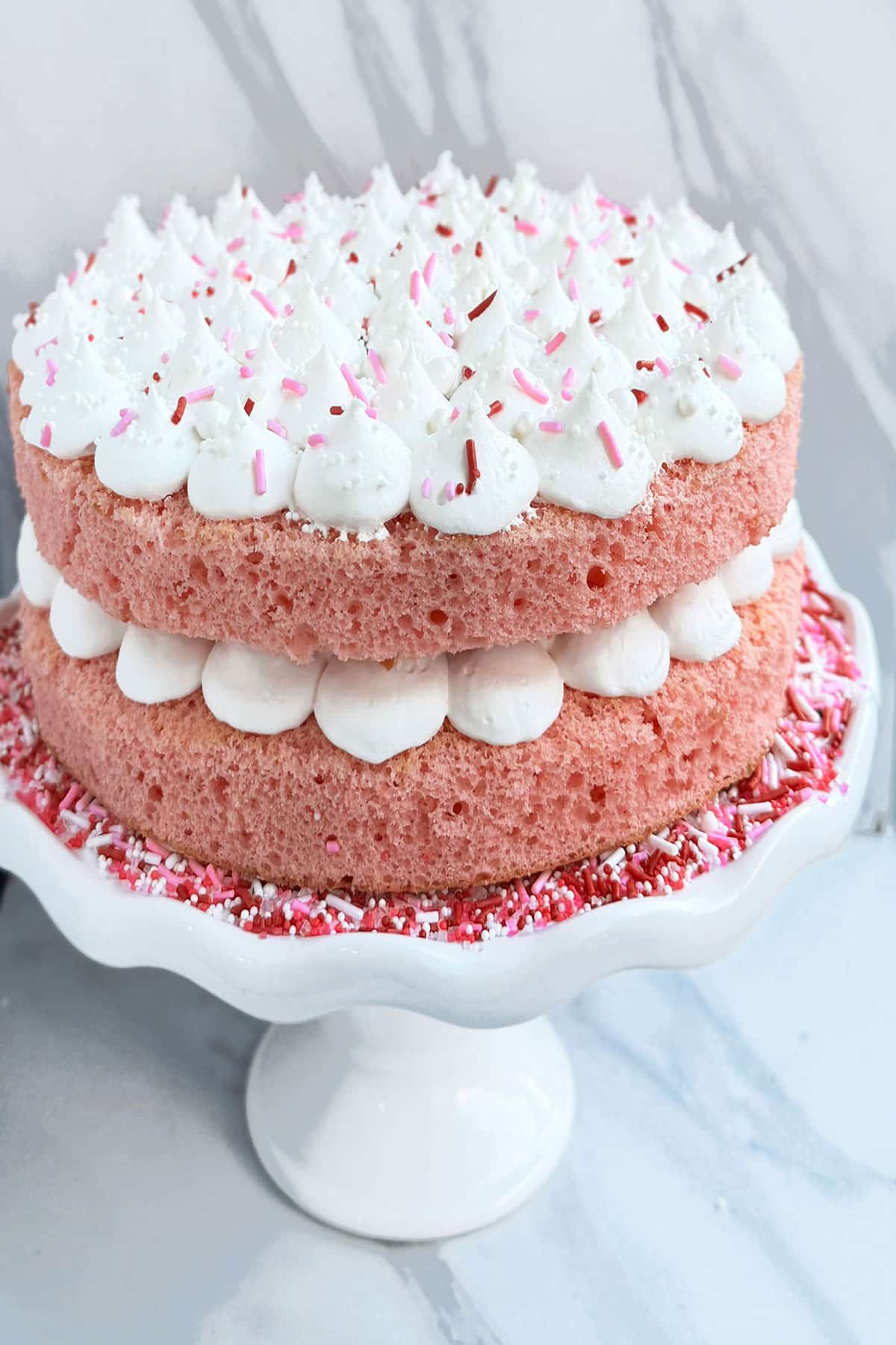 Easy Pink Champagne Cake From Scratch With Whipped Cream Frosting and Sprinkles on White Cake Stand. 