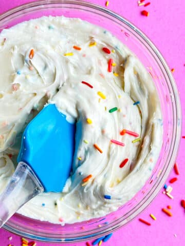 Easy Funfetti Frosting (Sprinkle Frosting) in Glass Bowl on Pink Background.