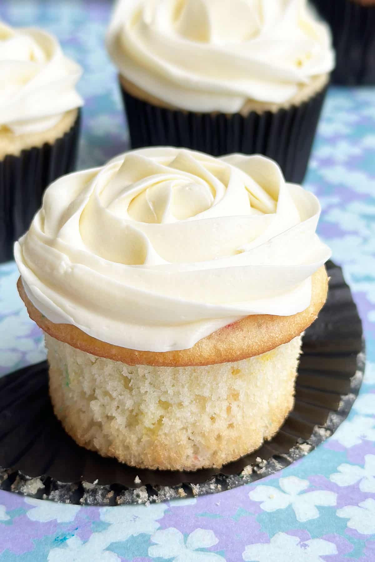 Easy Almond Cupcakes With Almond Buttercream Frosting on Blue Pattern Background- Liner Removed.